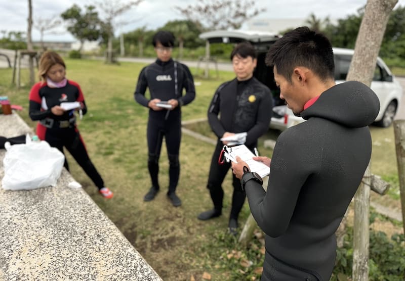 PADI IDC中、講師の指導のもと受講生が屋外でキューカードを読みながら準備を進めている様子