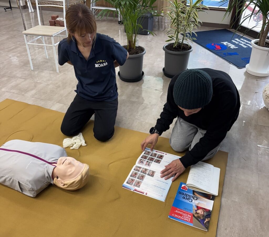 看護師スタッフの山崎光美が受講生と一緒にEFR教材を確認しながら応急処置の手順を指導している様子の写真。