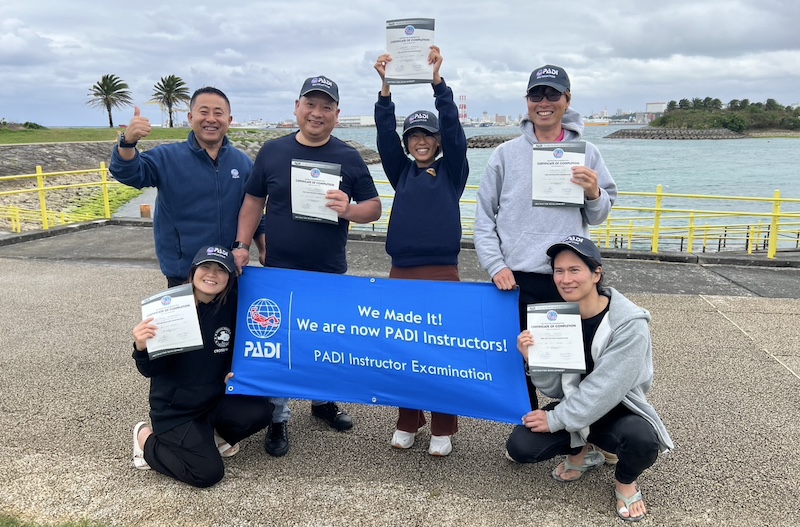 2025年3月のPADIインストラクター試験(IE)に合格した受講生1名が、他候補生とエグザミナーと笑顔の記念撮影をしている様子。